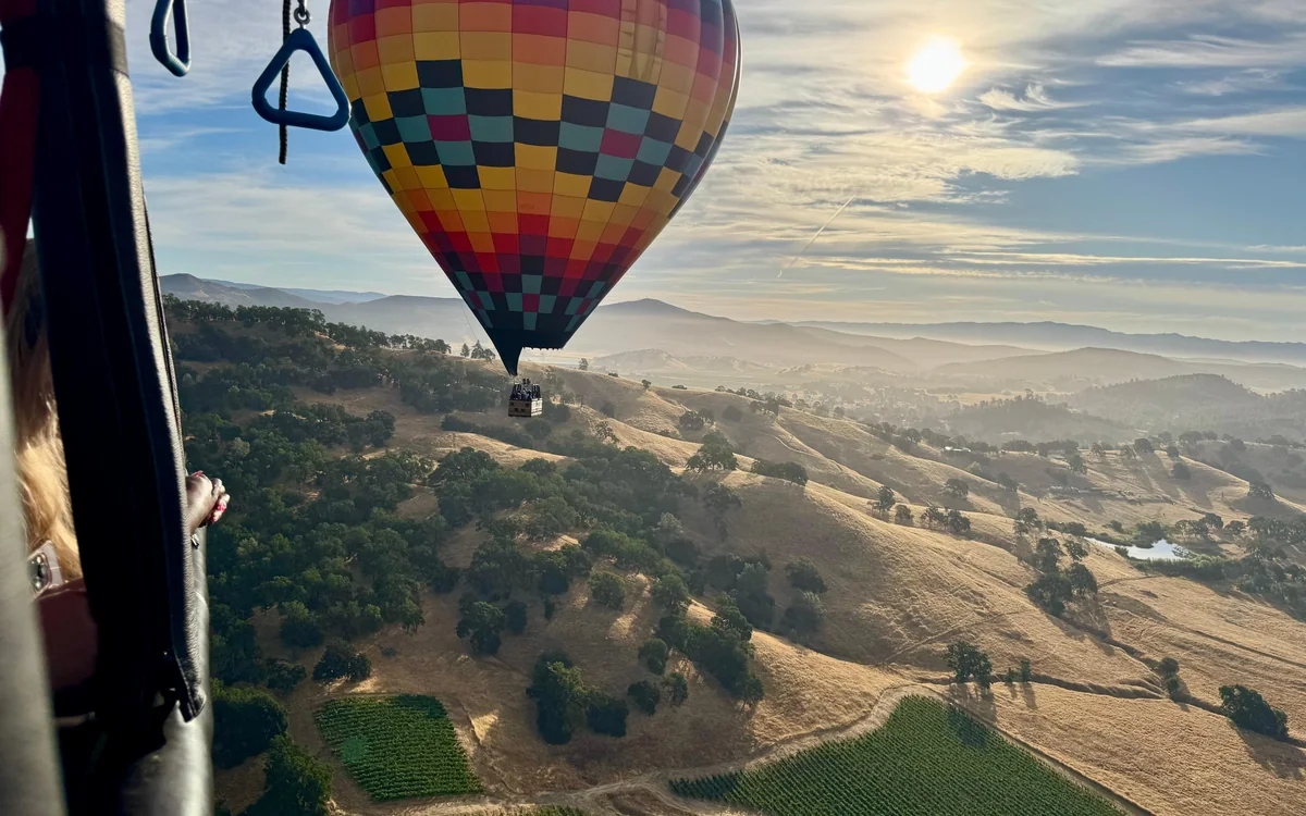 Un globo aerostático planeando bajo sobre hileras de viñas en el fondo de Napa Valley